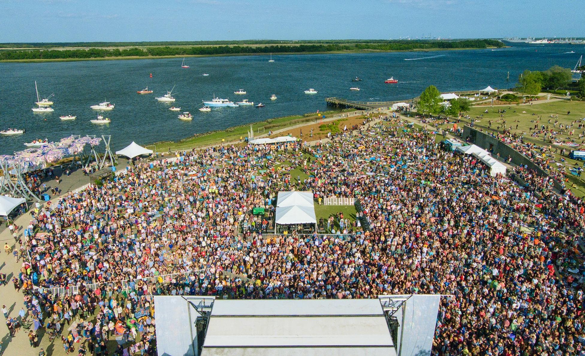Aerial view of the High Water Festival crowd filling a waterfront lawn beside the harbor