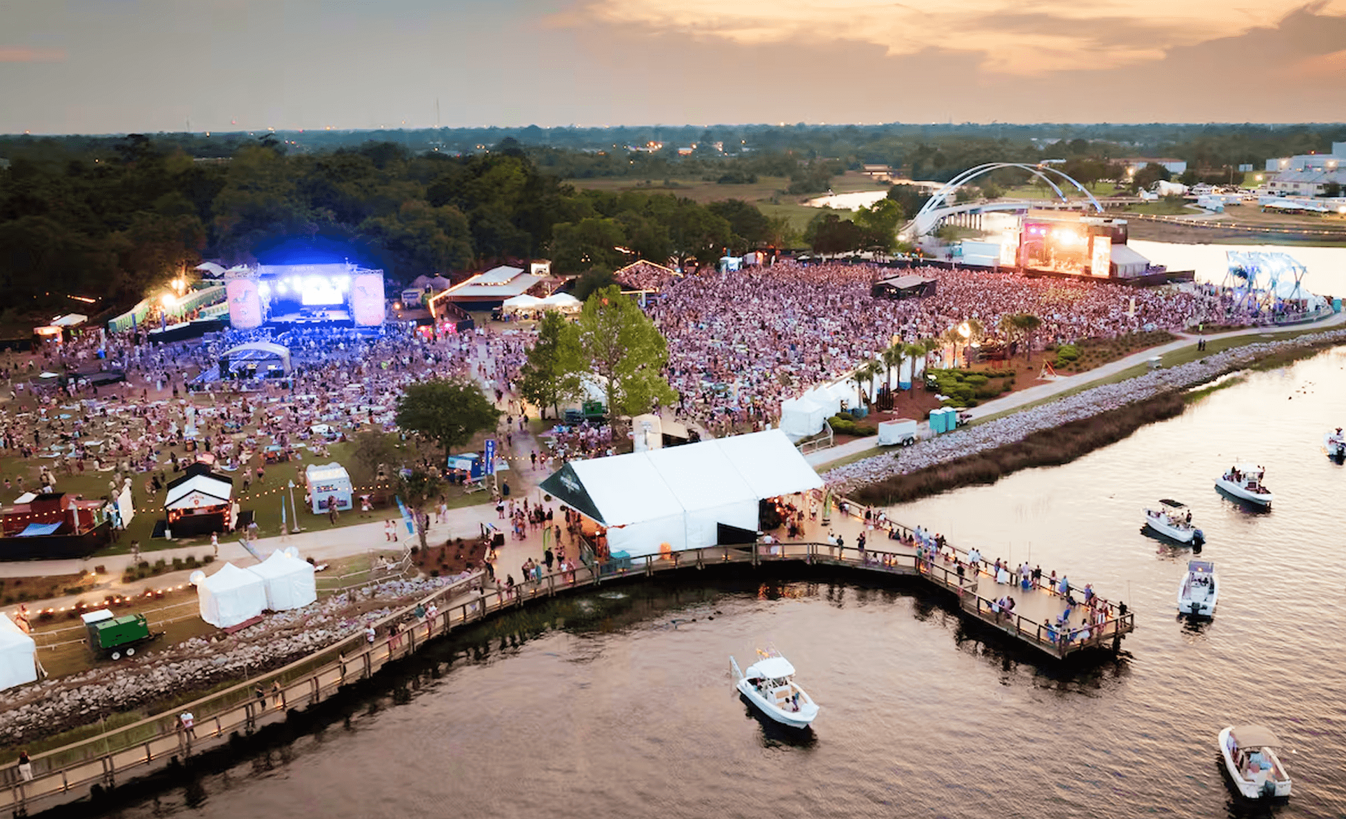 Aerial sunset view of High Water Festival with dual waterfront stages and a curving pier